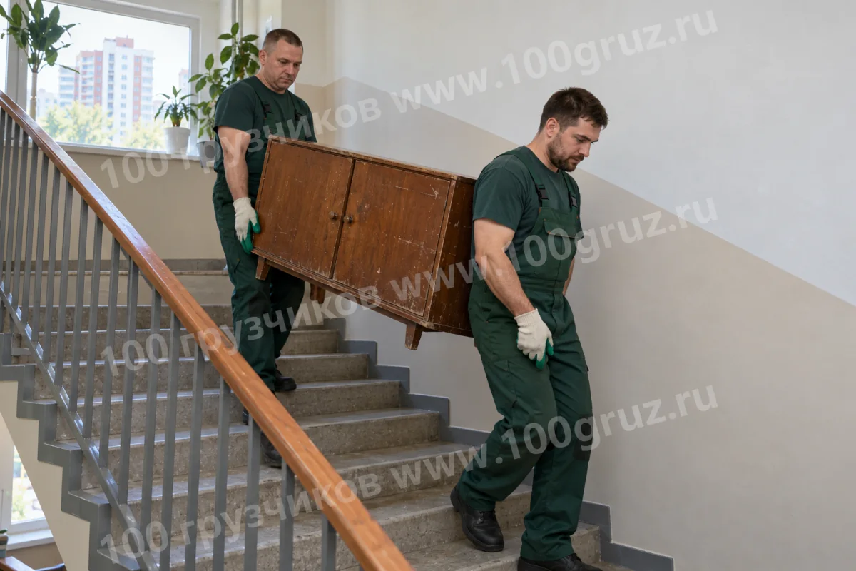 Два грузчика спускают старую деревянную тумбу по лестнице