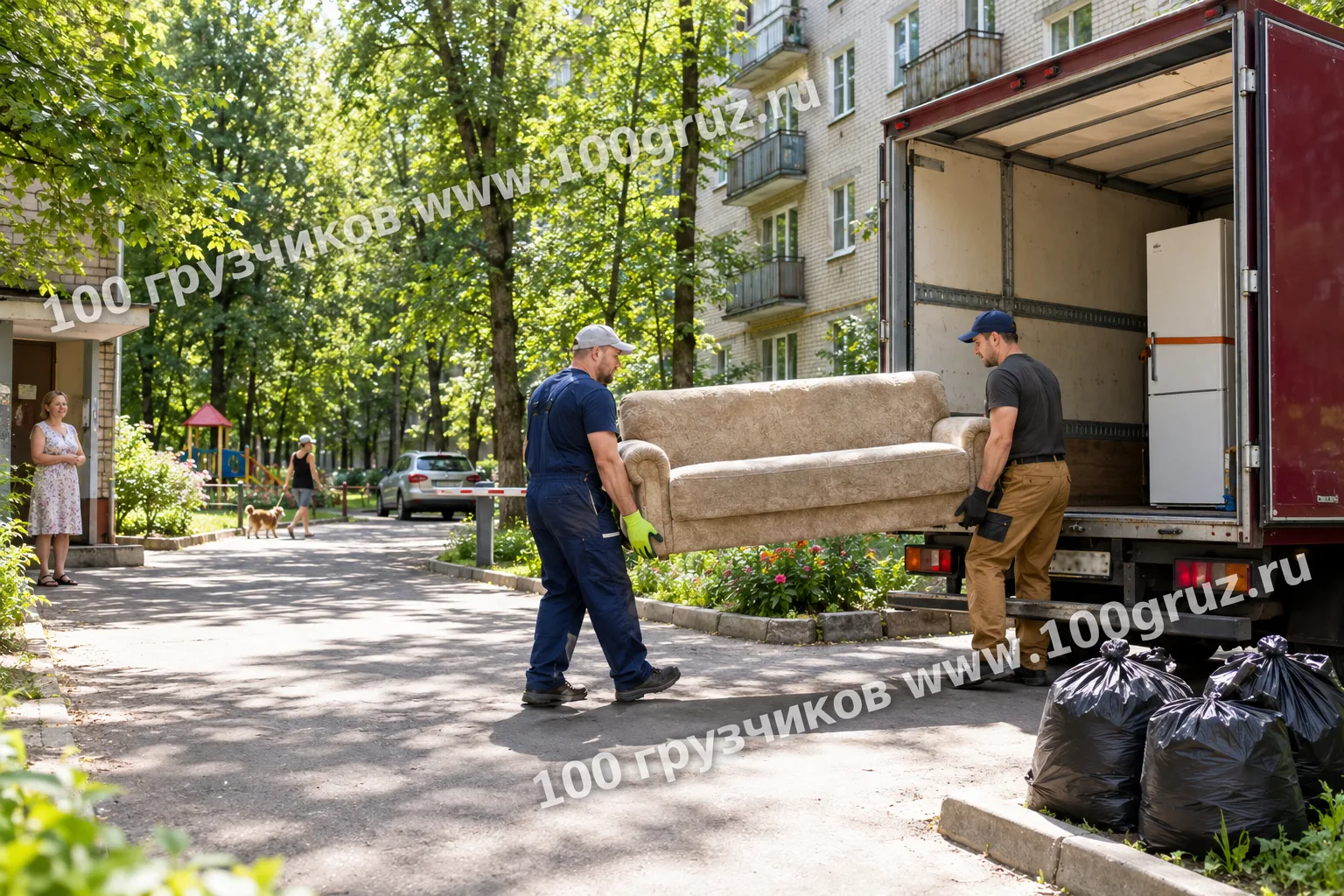 Грузчики несут старый диван к грузовой машине во дворе хрущёвки; в кузове холодильник, рядом мешки